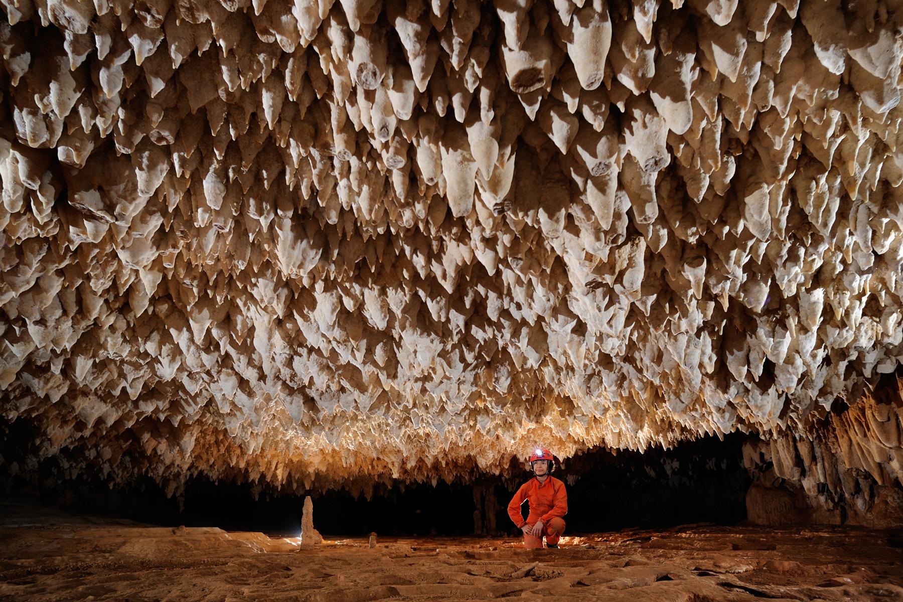 Cueva de Santa Catalina (Expédition Cuba 2012 - Team La Salle). Spéléo accroupi dans galerie au plafond bas concrétionné.