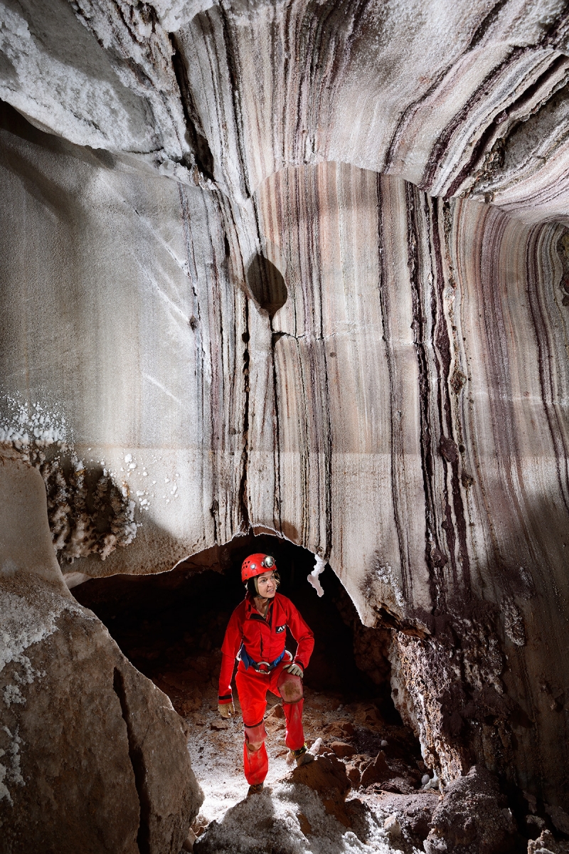 3N Cave (Iran, île de Qeshm, diapir de sel de Namakdan) - Entrée supérieure : spéléologue dans une porte naturelle dans des couches de sel colorées verticales