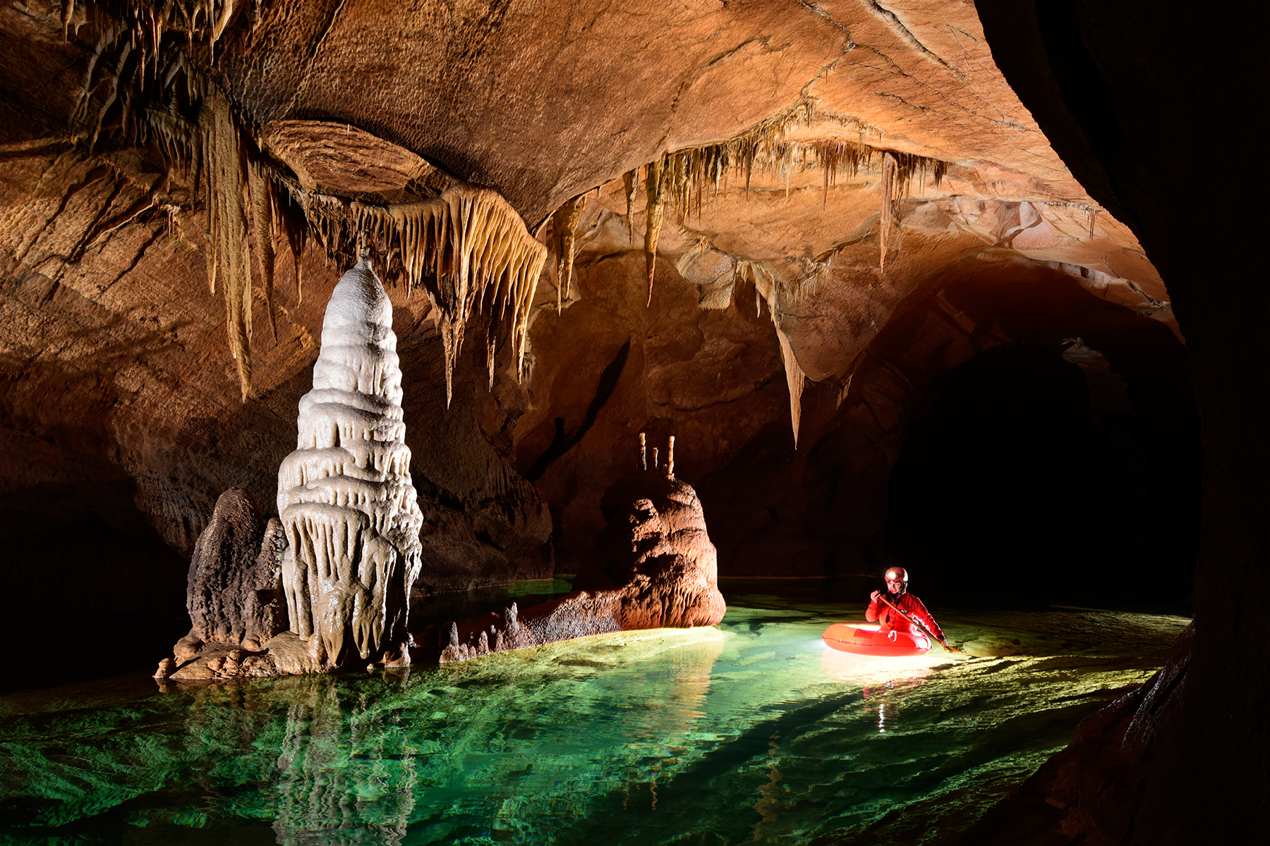 Krizna Jama (Slovénie) Spéléo progressant en canot dans une rivière souterraine aux eaux vertes avec grande stalagmitique blanche en premier plan (le sous-marin)