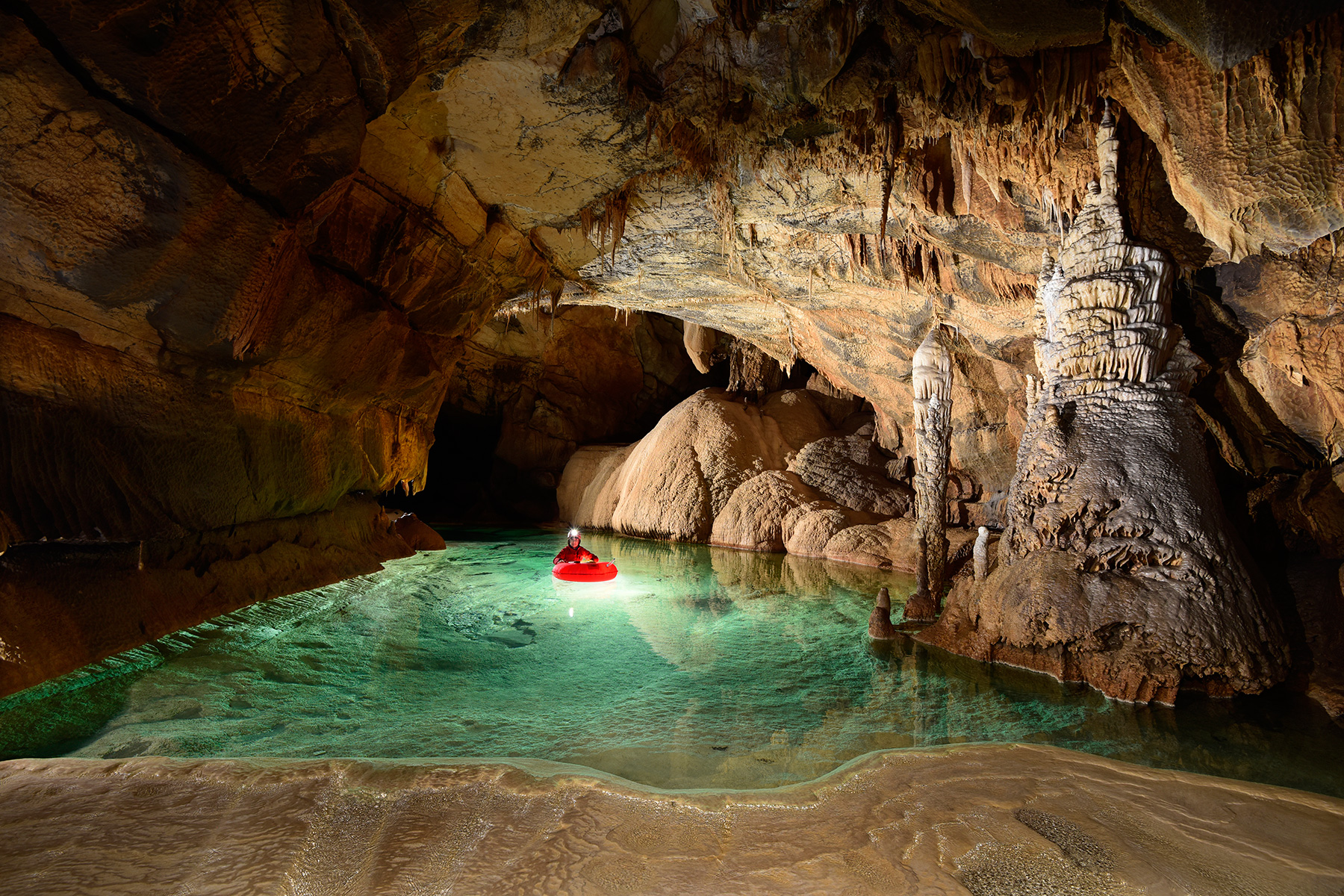 Krizna Jama (Slovénie) - Spéléo progressant en canot dans une rivière souterraine concrétionnée aux eaux vertes avec dépôts de calcite en premier plan