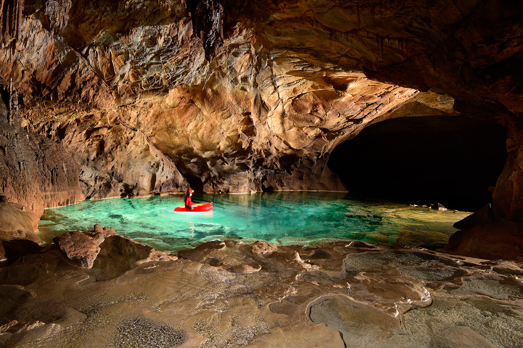 Krizna Jama (Slovénie) - Spéléo progressant en canot dans une rivière souterraine aux eaux vertes avec dépôts de calcite en premier plan