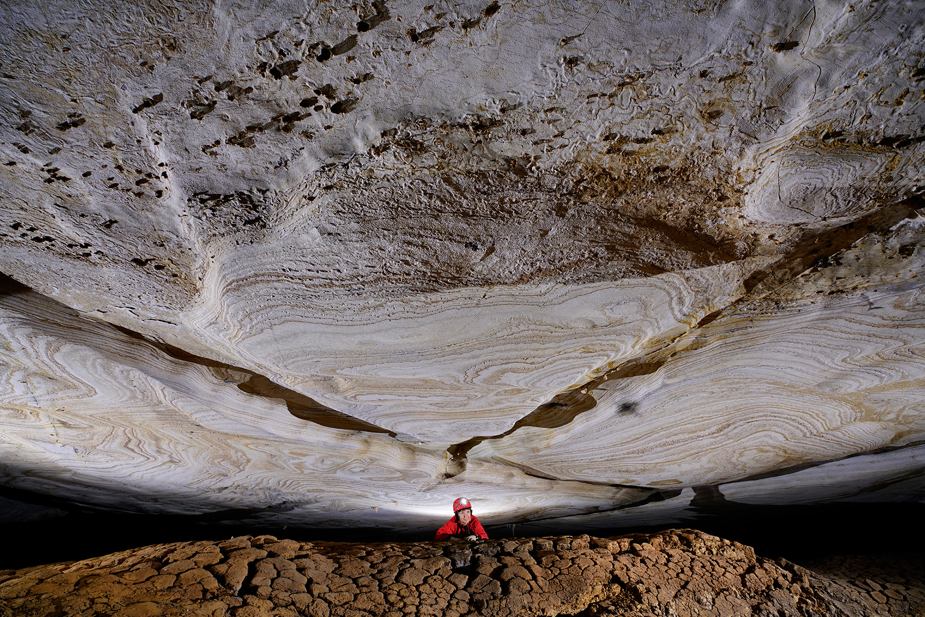Gruta de Lapa Doce (Iraquara, Bahia) - Spéléo débouchant entre un plafond blanc avec motifs et un sol de boue craquelée.