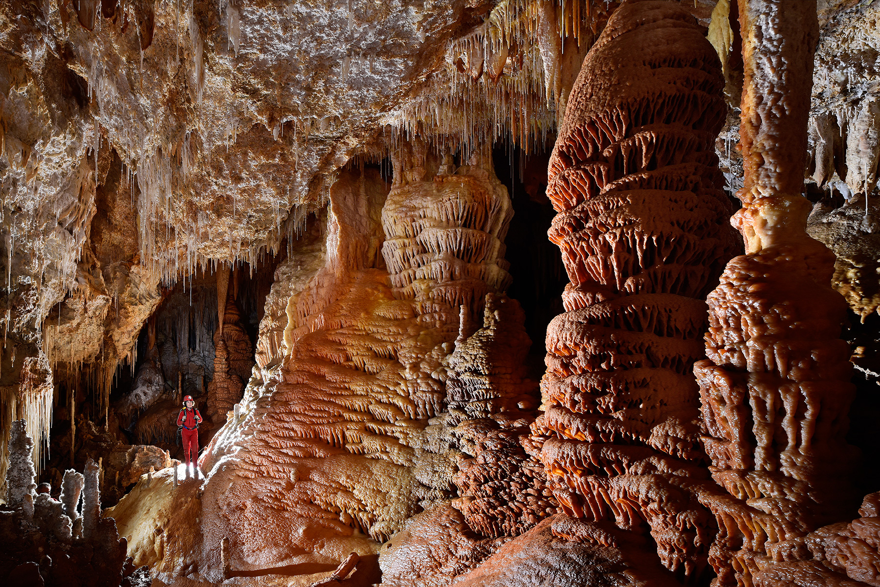 Grotte de Clamouse - Galerie concrétionnée avec coulées colorées et grandes colonnes rouges (spéléo en arrière plan)