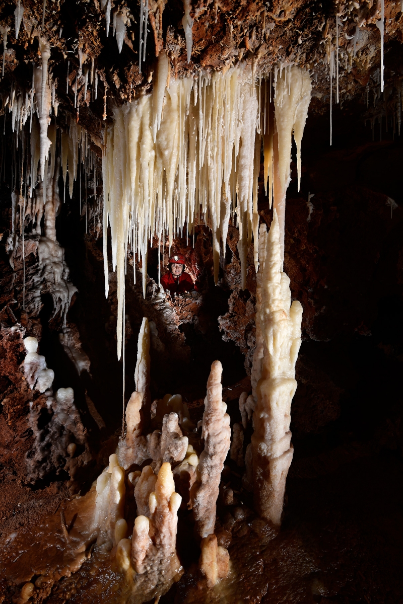 Grotte de Clamouse (partie non aménagée) - Rideau de stalagmites et stalactites avec spéléo dans une lucarne en arrière plan