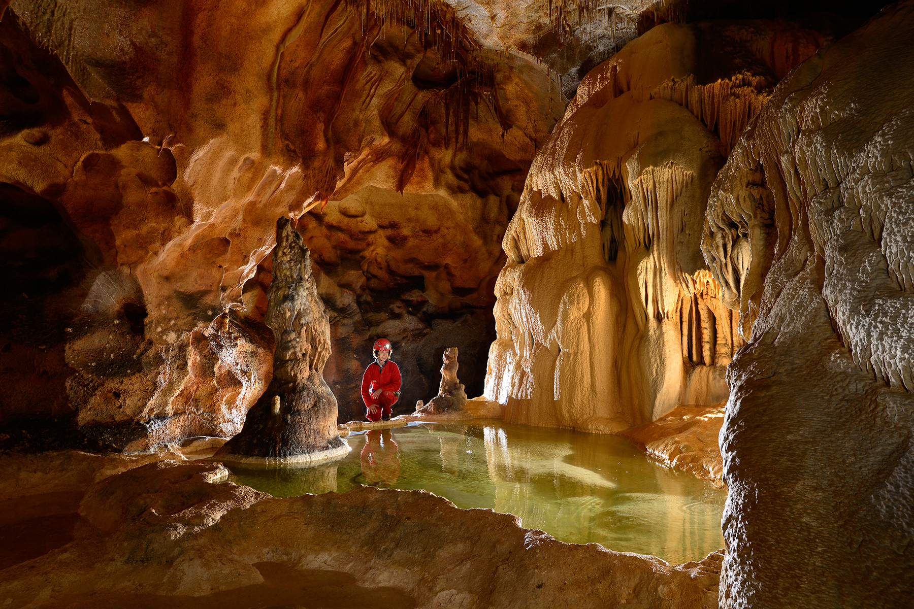 Grotte de Saint-Marcel (Ardèche) - Spéléo accroupie au bord d'un gour avec eau verte et concrétions