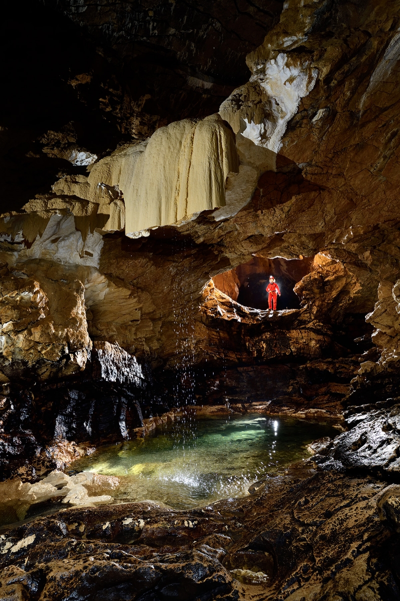 Grotte de Vallorbe (Suisse) - Petit lac alimenté par une cascade qui est à l'origine des dépôts de tufs. La coulée a probablement été cassée lors d'une  crue par l'eau arrivant sous pression par la conduite dans laquelle se trouve le personnage.