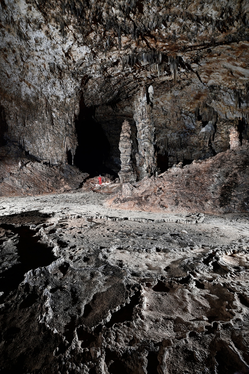 Slaughter Canyon Cave (USA - Nouveau Mexique) - Salle avec spéléo au pied de grandes stalagmites massives en fond et gour gris en premier plan