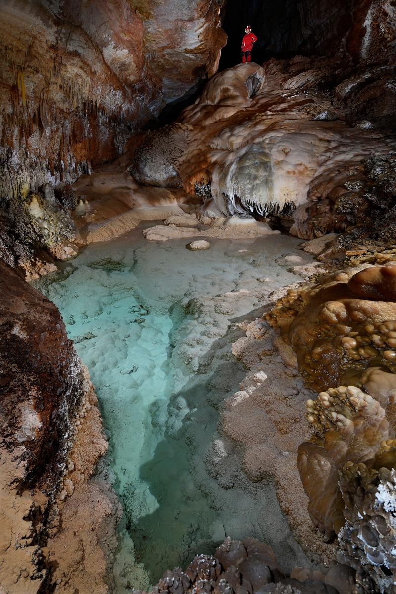 Hell Below Cave (USA - Nouveau Mexique) - Petit lac cristallisé aux eaux turquoise avec coulées de calcite l'entourant et spéléo en fond