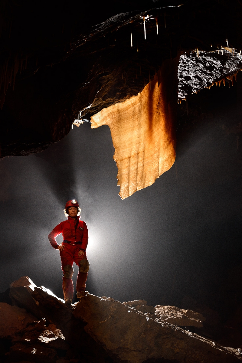 Grotte de Han (réseau sud) - Salle de la Pentecôte : spéléo devant une grande draperie orange translucide 