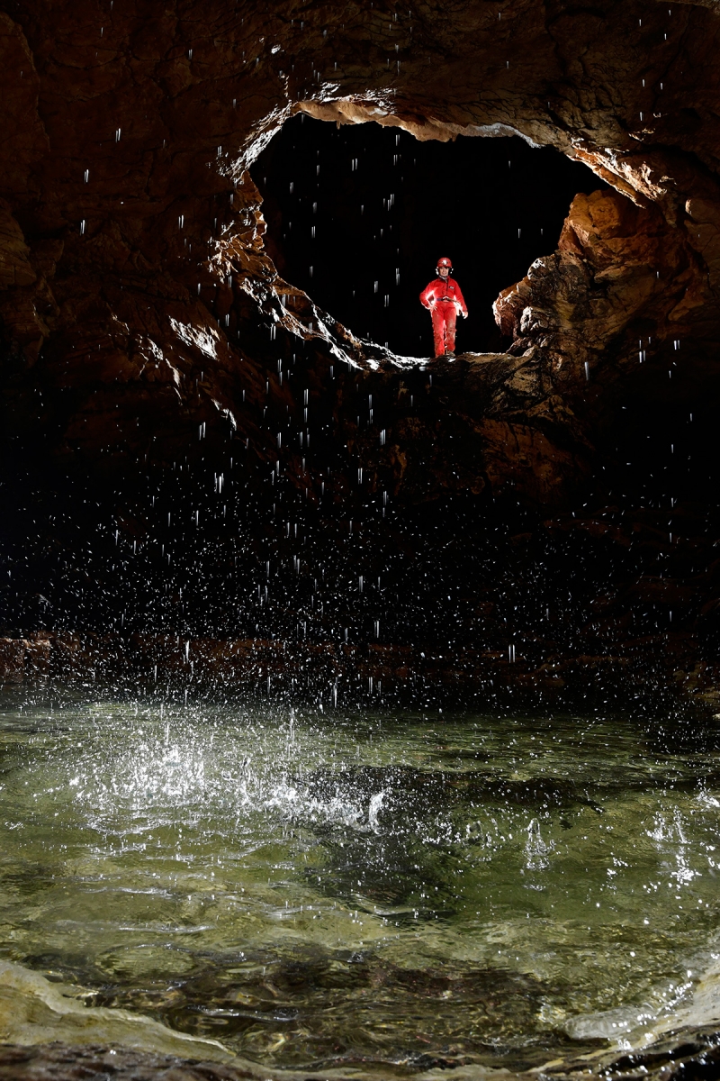 Grotte de Vallorbe (Suisse) - Eau d'une petite cascatelle éclatant dans une vasque avec spéléo en arrière plan dans le conduit de la galerie