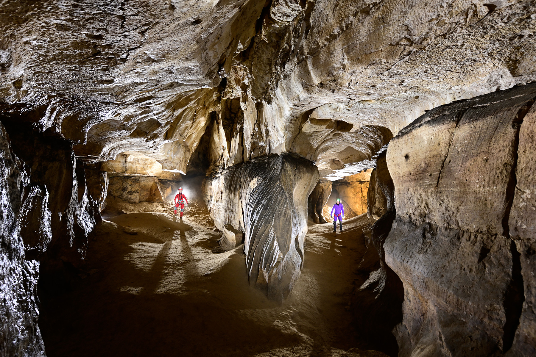 Grotte des Cavottes (Doubs) - Galerie large faisant un méandre (deux spéléos en arrière plan dans chaque partie)