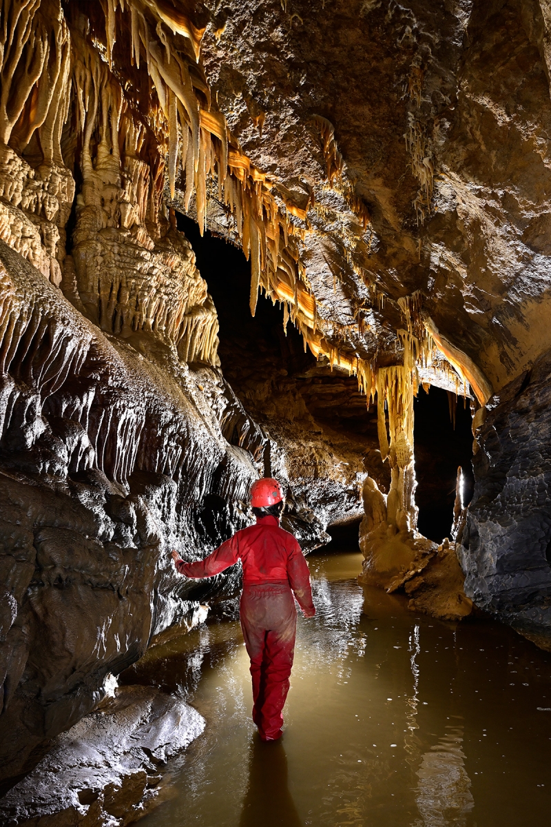 Grotte du Crotot (Doubs) - Spéléo de dos dans galerie avec rivière et concrétions