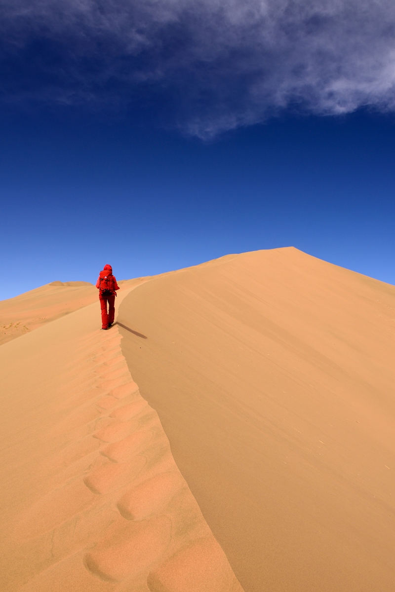 Désert du Badain Jaran (Chine, Mongolie Intérieure) - Randonneuse en rouge marchant sur la crête d'une dune