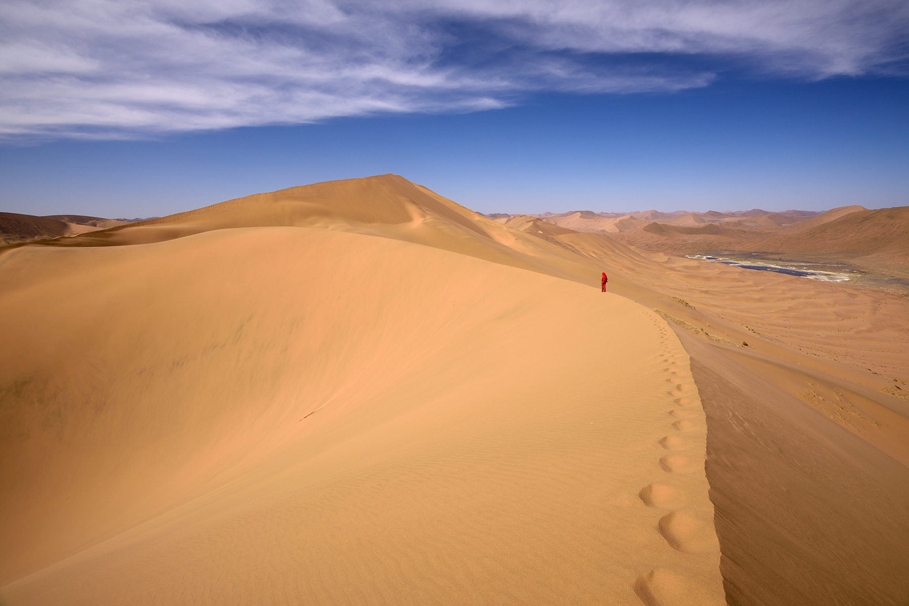 Désert du Badain Jaran (Chine, Mongolie Intérieure) - Vue générale d'un enchaînement de dunes avec randonneuse sur la crête. Vallée avec lac salé à droite.