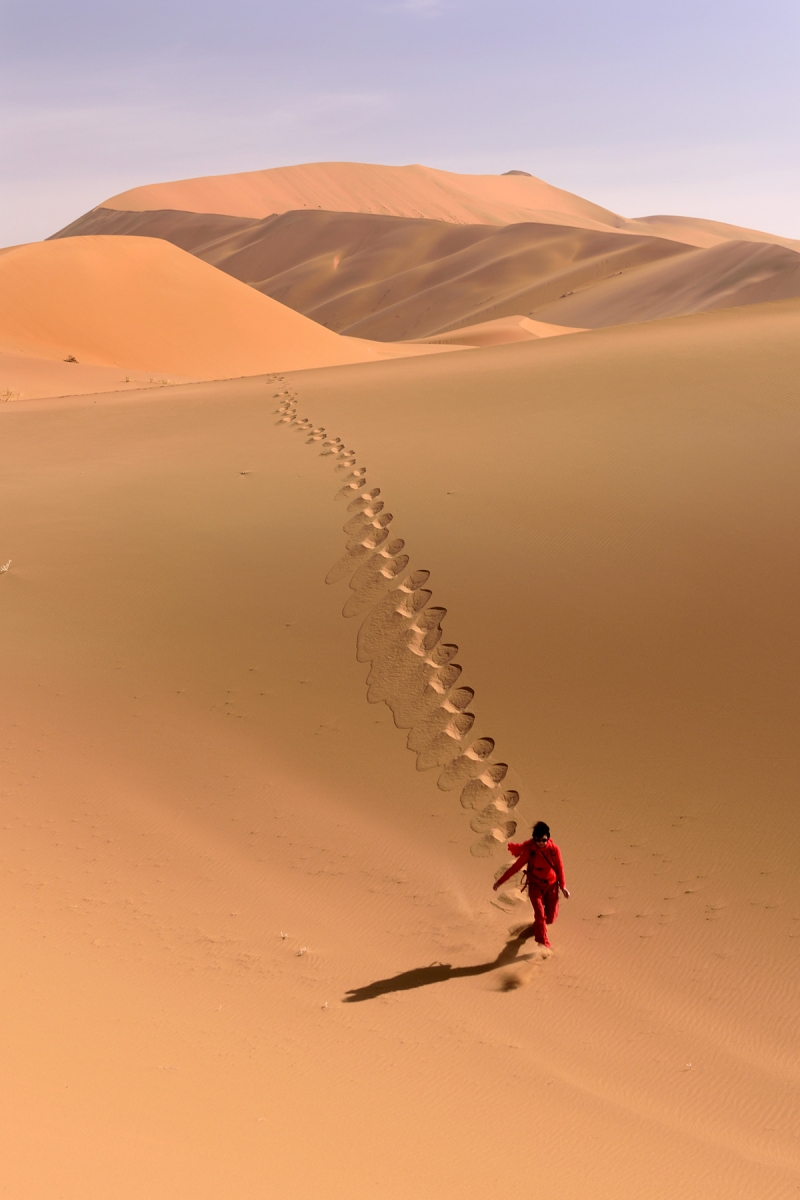Désert du Badain Jaran (Chine, Mongolie Intérieure) - Randonneuse en rouge marchant dans les dunes près de Bilutu