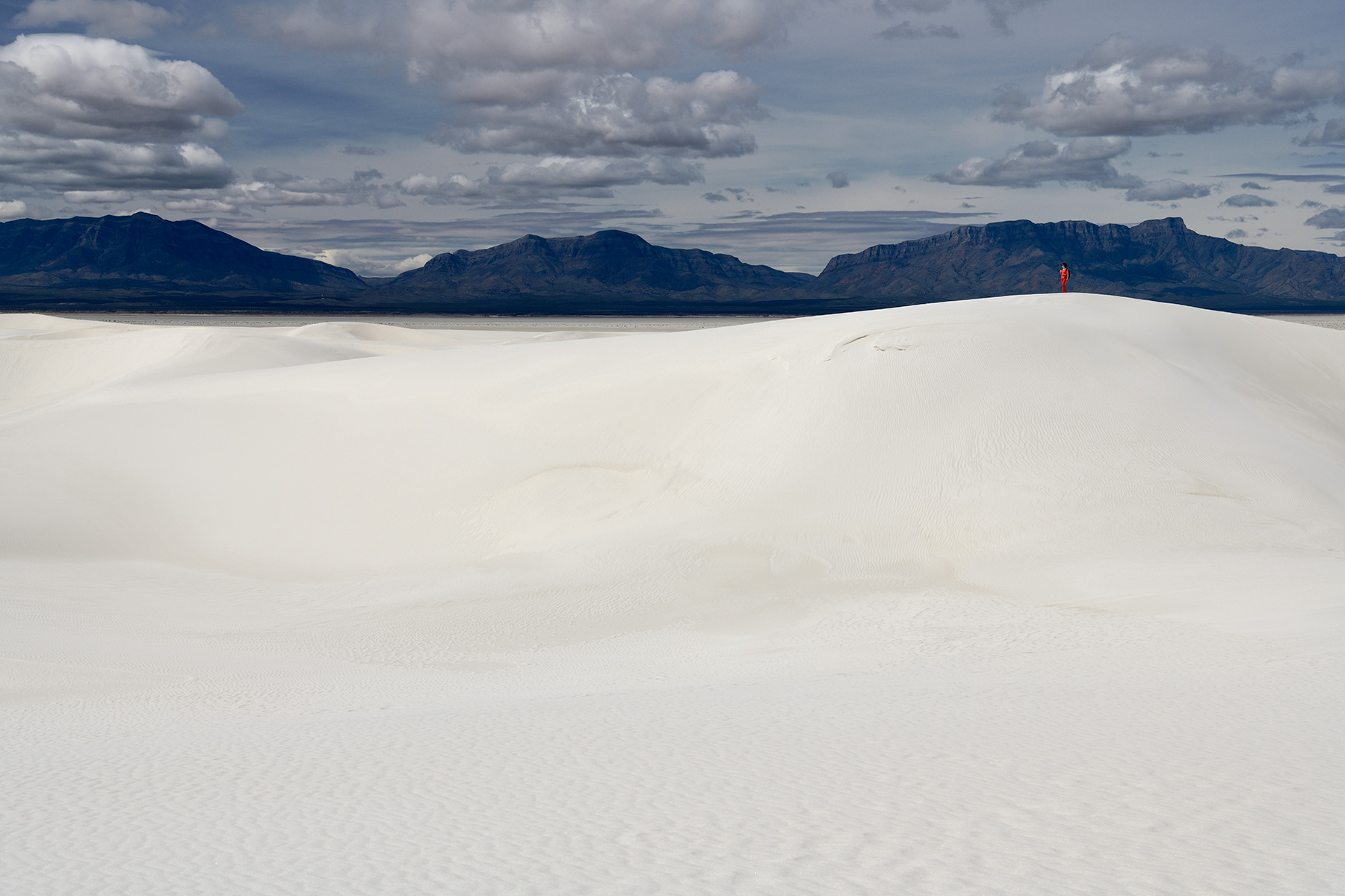 White Sands National Park (Nouveau Mexique, USA) - Dunes de sable blanc avec personnage en rouge sur la crête et montagnes sombres en fond