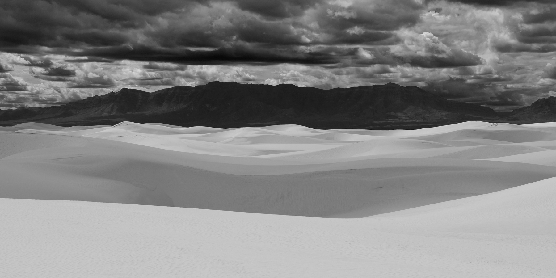 White Sands National Park (Nouveau Mexique, USA) - Jeux de lumière et d'ombre sur les dunes de sable blanc avec montagne sombre en fond et ciel nuageux (photo noir & blanc)