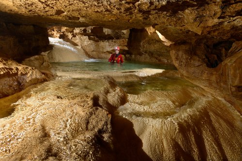 Grotte de Coufin-Chevaline - Progression dans la rivière : spéléo dans une vasque avec sol recouvert de calcite au premier plan(SP-14-0187)