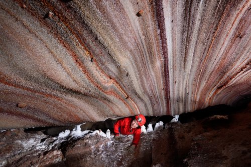 3N Cave (Iran, île de Qeshm, diapir de sel de Namakdan) - Entrée supérieure : spéléo passant une étroiture avec des couches de sel colorées au plafond (blanc, rose, orangé, rouge)(SP-16-0030)