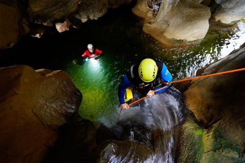 Clue de Terminet (Aude) : cascade de la grotte - Stage photo canyon des 11 et 12 juin 2016. Cette partie souterraine du canyon a été exploitée pour l'utilisation de flashs électroniques déclenchés par des cellules radio. Le premier flash électronique est tenu par le canyoniste dans la vasque avec un éclair dirigé vers le fond (pleine puissance). Le second est placé latéralement à gauche pour éclairer légèrement le fond. Le premier canyoniste est éclairé par la lumière du jour. La photo a été réalisée au 1/15ème de seconde (main levée) à f6 pour une sensibilité de 640 ISO. (MO-16-0042.jpg)