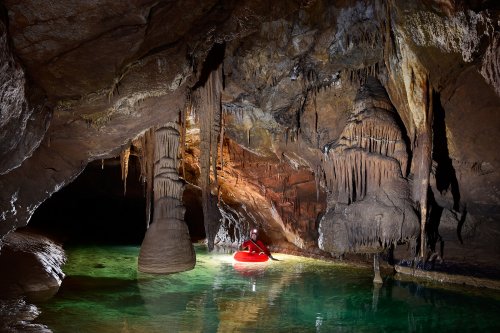 Krizna Jama (Slovénie) - Spéléo progressant en canot dans une rivière souterraine concrétionnée aux eaux vertes - pilier s'arrêtant à la surface de l'eau(SP-17-0424)