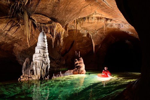 Krizna Jama (Slovénie) Spéléo progressant en canot dans une rivière souterraine aux eaux vertes avec grande stalagmitique blanche en premier plan (le sous-marin)(SP-17-0418)
