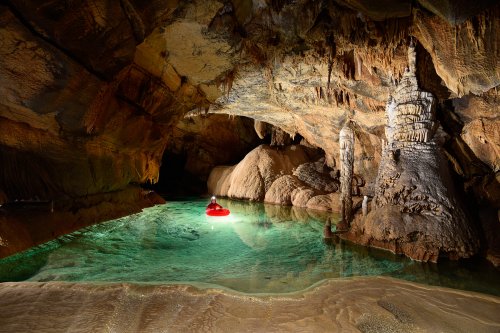 Krizna Jama (Slovénie) - Spéléo progressant en canot dans une rivière souterraine concrétionnée aux eaux vertes avec dépôts de calcite en premier plan(SP-17-0409)