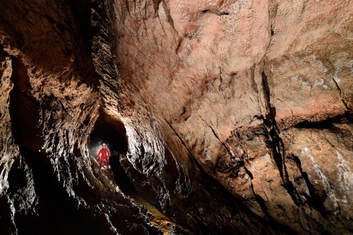 Grotte de Pont de Ratz (Hérault) - Paroi de calcaires roses avec des dépôts de remplissage (spéléo contre-jour dans la galerie en arrière plan)(SP-19-0010)