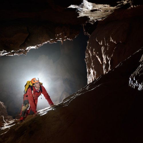 Grotte du sergent (Hérault) - Jeune femme au début de la remontée d'une pente glaiseuse. Le but de cette photo était de montrer qu'on peut faire un cliché intéressant sans sujet. L'important est de créer une ambiance. Dans le cas présent, trois flashs ont été mis en contre-jour pour entourer le modèle d'un halo de lumière et il lui a été demandé de simuler l'escalade de la pente. (SP-19-2097)