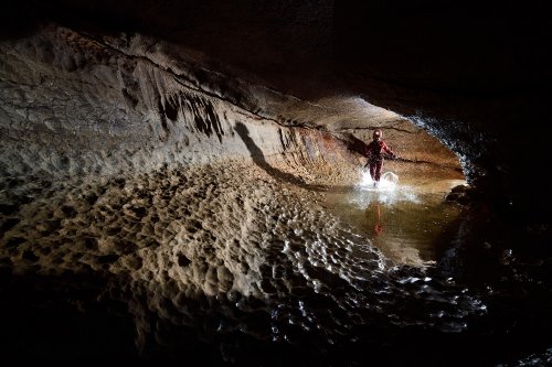 Event de Peyrejal (Ardèche) - Spéléo traversant une vasque en courant dans une galerie en conduite forcée (éclaboussures)(SP-20-0135)