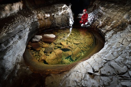 Goule Sauvas (Ardèche) - Vasque dans la galerie d'entrée avec spéléo accroupie(SP-20-0138)