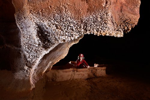 Grotte de Saint-Marcel d'Ardèche (réseau IV) - Paroi couverte de petites boules de calcite blanche avec spéléo dans un gour en arrière plan(SP-22-2109)