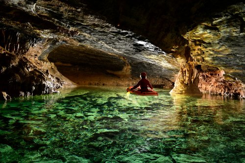 Grotte de la Cabane de Saint-Paul des Fonts (Aveyron) - Spéléo traversant en canot un petit lac (personnage non éclairé)(SP-23-1548)