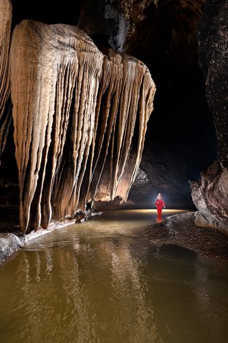 Grotte de Tham Nam Hoo (province de Mae Hong Son, Thaïlande) - Spéléo à côté d'une alignement de draperies géantes au dessus de la rivière (vue de l'amont avec draperies claires) (SP-24-0521)