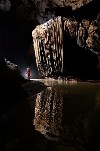 Grotte de Tham Nam Hoo (province de Mae Hong Son, Thaïlande) - Spéléo à côté d'une alignement de draperies géantes au dessus de la rivière (vue d' ensemble de l'aval très sombre avec reflet dans l'eau) (SP-24-0383)