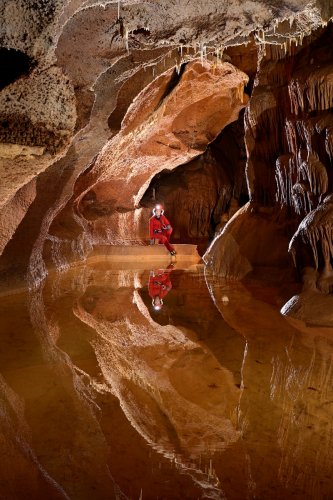 Grotte de Saint-Marcel d'Ardèche (réseau I) - Gour avec spéléo assis dans le fond sur la barrière (reflet dans l'eau) (SP-24-2462)