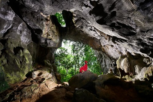 An Tho Thôn cave (Tan Hoa, Vietnam) - Porche d'entrée vu de l'intérieur avec personnage assis sur rocher.(SP-25-0107)