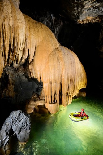 Hang Va cave (Phong Nha, Vietnam) - Spéléo dans canot pneumatique sur la rivière au pied d'un grande coulée de calcite orange(SP-25-0352)