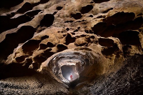 Grotte de la Douch (Courniou, Hérault) - Galerie finale avec personnage éclairé en fond et talus d'argile éclairés sur les côtés.(SP-25-0664-B)
