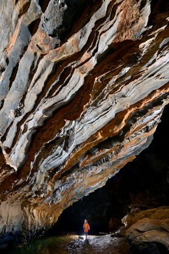 Caverna da Agua Suja (Sao Paulo, Brésil) - Grande paroi de calcaire  avec des  bandes orange en relief au dessus de la rivière (spéléo en fond)(SP-25-2198)