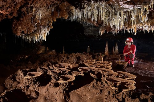Caverna Angelica (Goias, Brésil) - Spéléo dans un passage bas avec plafond concrétionné et coupelles de calcite recouvertes d'argile au sol.(SP-25-1575)