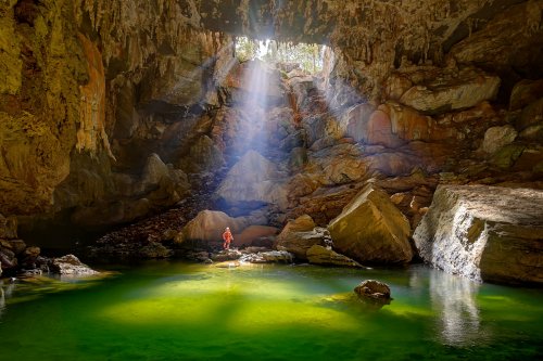 Lapa Terra Ronca (Goias, Brésil) - Rayons de soleil éclairant la rivière aux eaux vertes à partir d'un orifice (eau verte en premier plan et spéléo sur rocher à la base du gouffre). Format horizontal.(SP-25-2012)