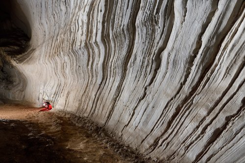 Gruta da Cerquinha ( Mato Grosso, Brésil) - Parois de calcaire blanc aux strates visibles avec personnage émergeant d'un passage bas dans le fond(SP-19-1263)