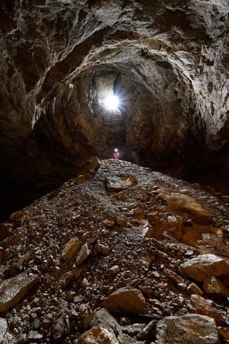 Gouffre des Ravières (Doubs) - Grand cône d'éboulis à la base du puits d'entrée éclairé en contre jour par la lumière du jour (spéléo perché sur le cône)(SP-20-0354)