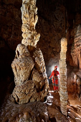 Aven du Mas de Rouquet (Hérault) - Pied de l'Obélisque dans la salle finale avec personnage derrière une stalagmite(SP-21-0161)