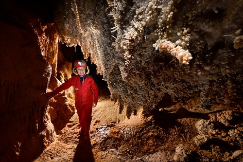 Grotte du Gard - Grande concrétion cylindrique horizontale  hérissée de cristaux de calcite avec spéléo en arrière plan(SP-23-1501)
