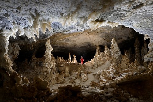 Grotte d'Hushm-Oyeek (Turkménistan) - Grande salle concrétionnée avec stalagmites de gypse, cristaux blancs au plafond et personnage en fond.(SP-24-1123)