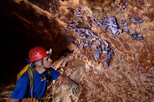 Grotte de Geophysicheskaya (Turkménistan) - Galerie rouge : personnage observant des cristaux de fluorite (fluorure de calcium) sur une paroi.(SP-24-1222)