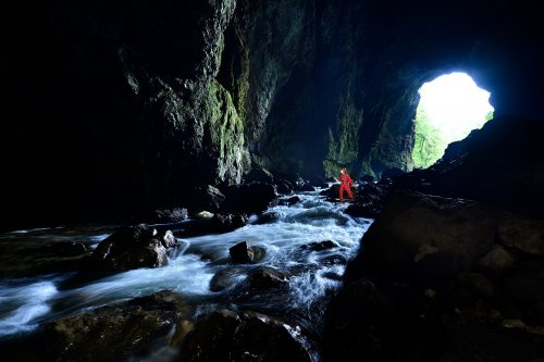 Tkalca Jama (Slovénie) - Spéléo progressant dans la rivière souterraine avec porche d'entrée en fond(SP-24-1814.)