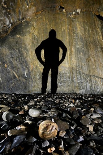 Gouffre de la Pierre Saint-Martin (Pyrénées-Atlantiques) - Plage de galets à la base de la salle de la Verna : gros galet rond en premier plan avec ombre d'un spéléo an arrière plan(SP-24-2201)